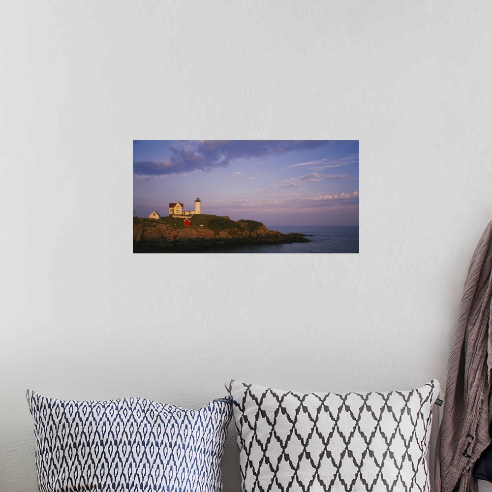 A bohemian room featuring Cape Neddick Lighthouse perched on the top of a green and rocky cliff with the warm sunset reflec...