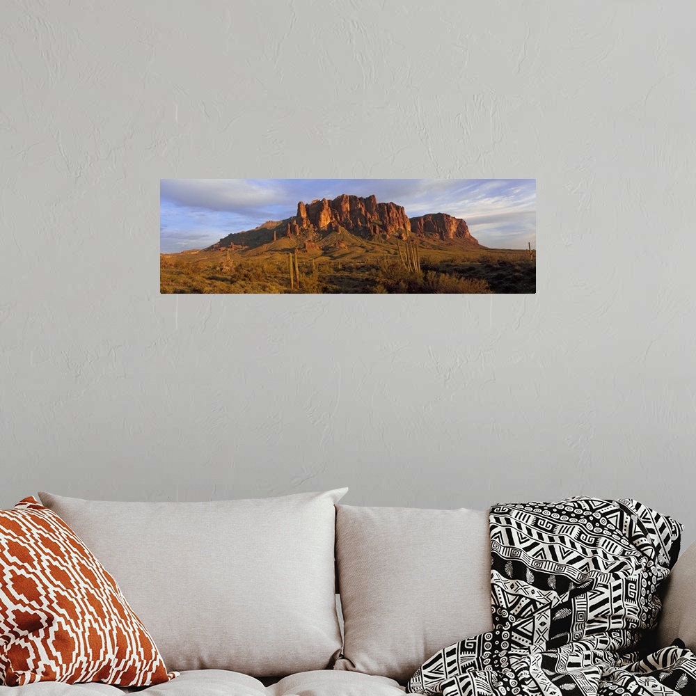 A bohemian room featuring An immense rock formation is photographed from a distance with green land in front of it that is ...