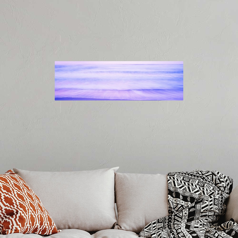 A bohemian room featuring A large panoramic picture taken of waves that are about to hit the beach with a dusk like sky abo...