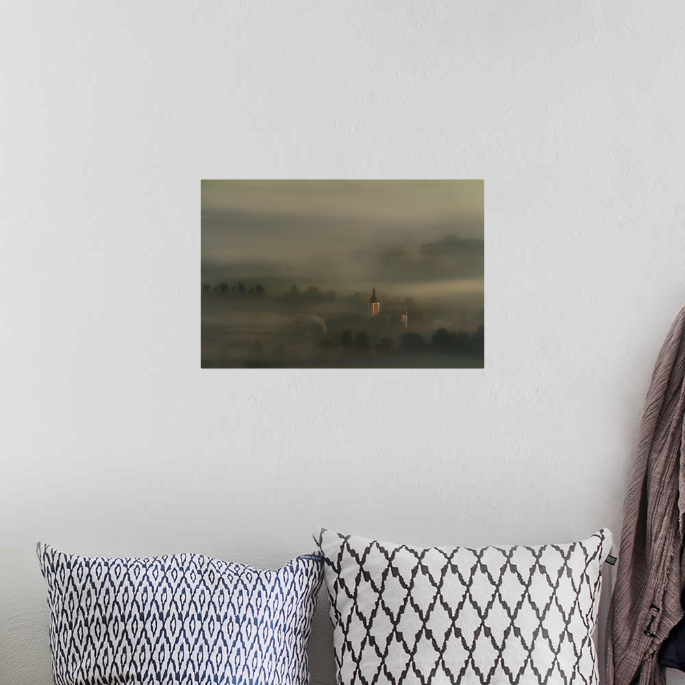 A bohemian room featuring Church spire rising through the thick blanket of fog that covers this countryside scene.