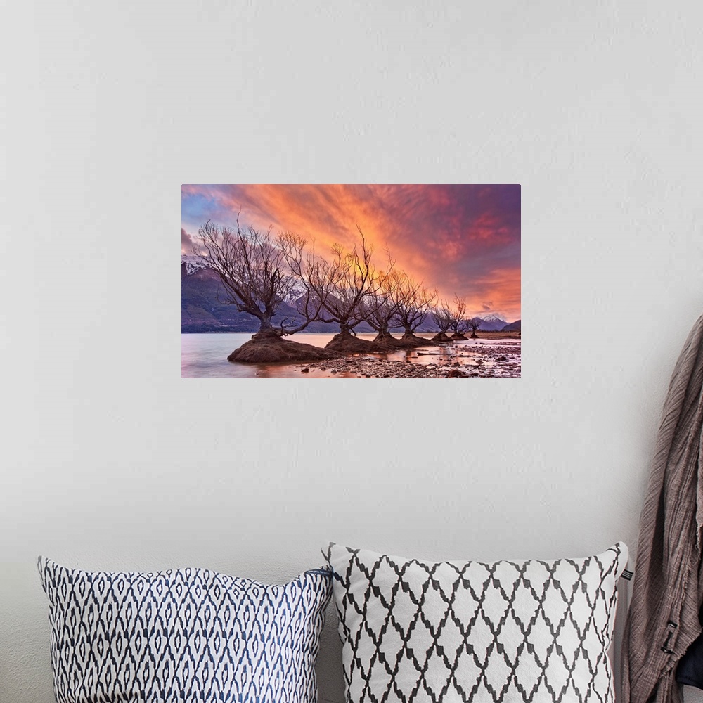 A bohemian room featuring A photograph of a row of bare branched trees in mud patches under an orange sky with mountains in...