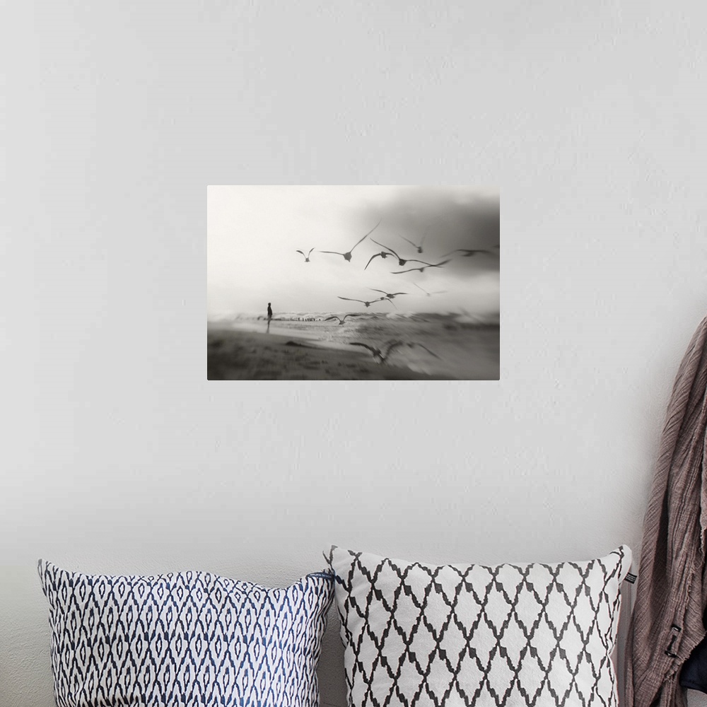 A bohemian room featuring A person standing on the shore with a flock of seagulls in flight.