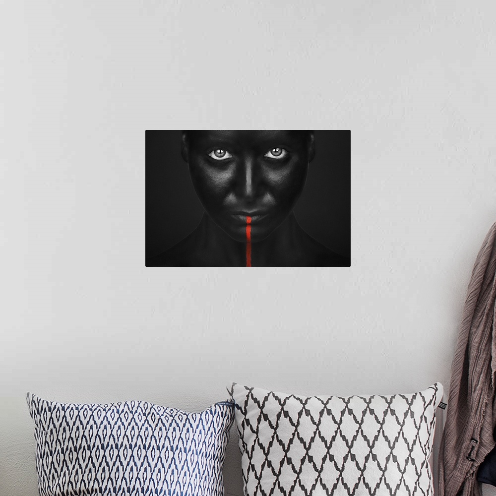 A bohemian room featuring A person with completely black bodypaint covering their face with a single red stripe running dow...