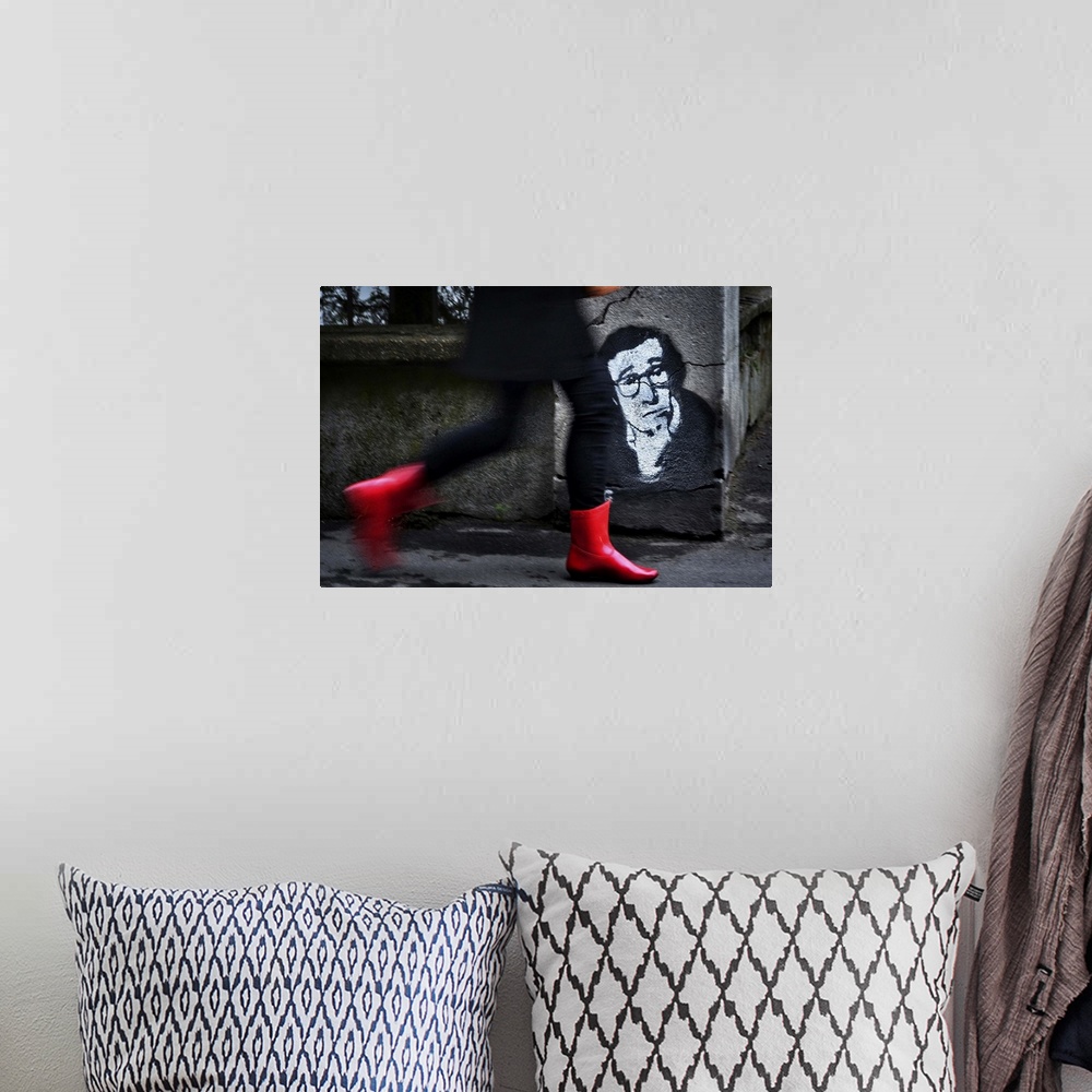 A bohemian room featuring A woman in red boots walks quickly down a street past a stenciled image of Woody Allen on a concr...