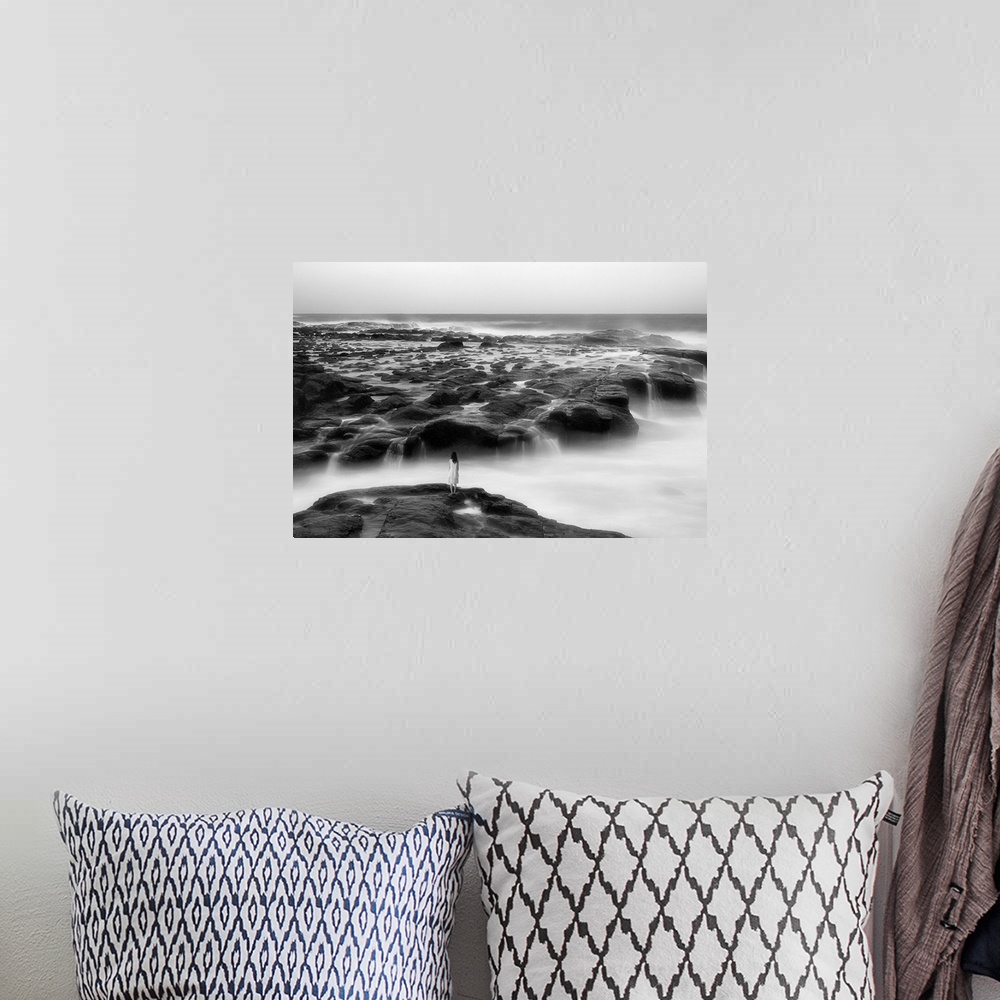 A bohemian room featuring A woman standing on the edge of a rocky shore by the ocean.