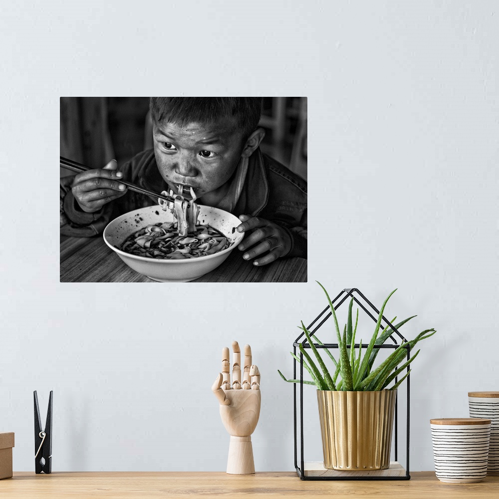 A bohemian room featuring A young boy eats a bowl of noodles with chopsticks.