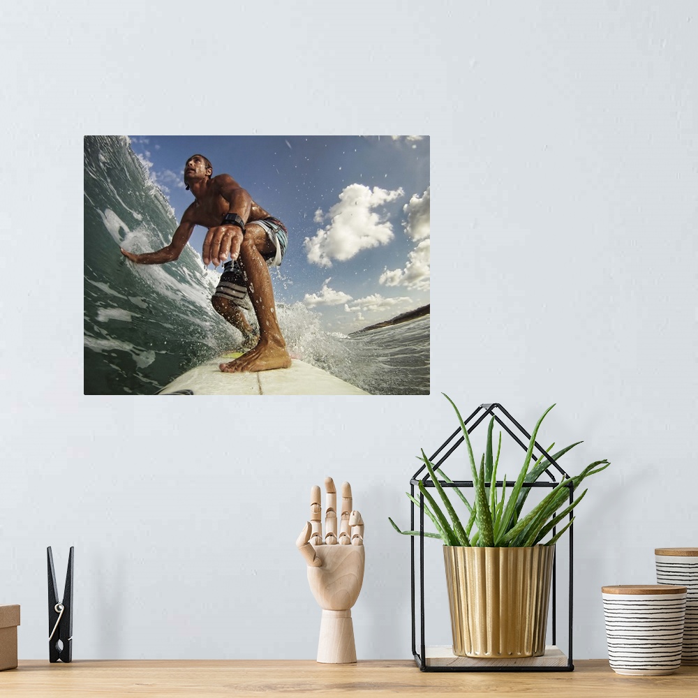 A bohemian room featuring A man on a surfboard rides a wave and touches the water with his outstretched hand on a sunny day.