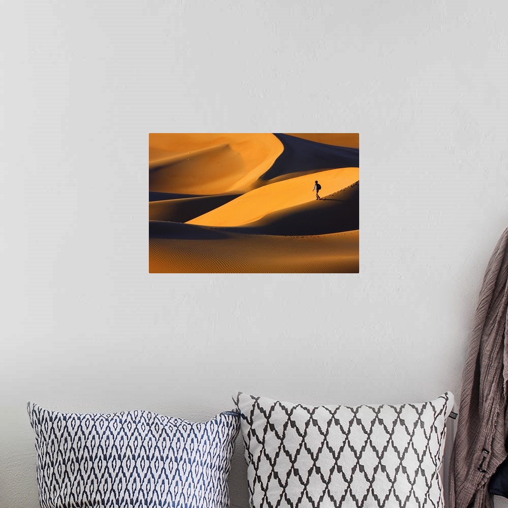 A bohemian room featuring A person walks on a sand dune in a golden desert at sunset.