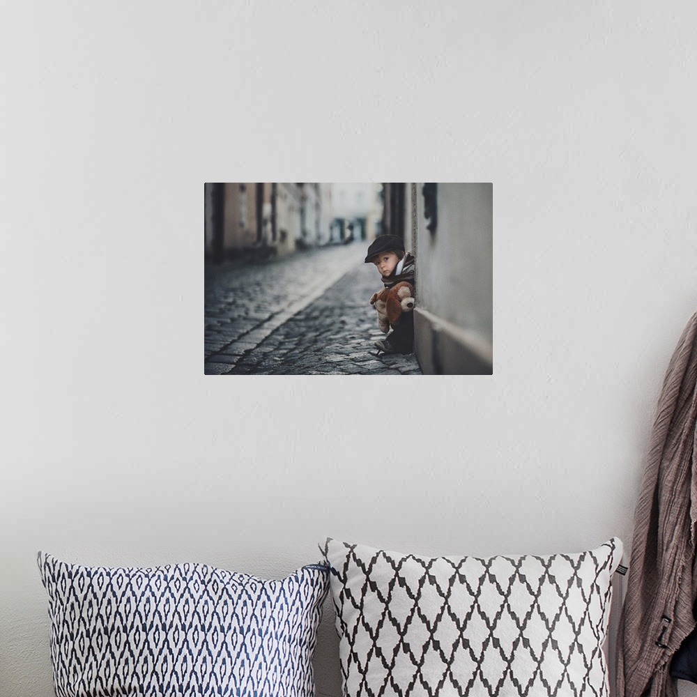 A bohemian room featuring A portrait of a little boy sitting on a doorstep on a cobblestone road.