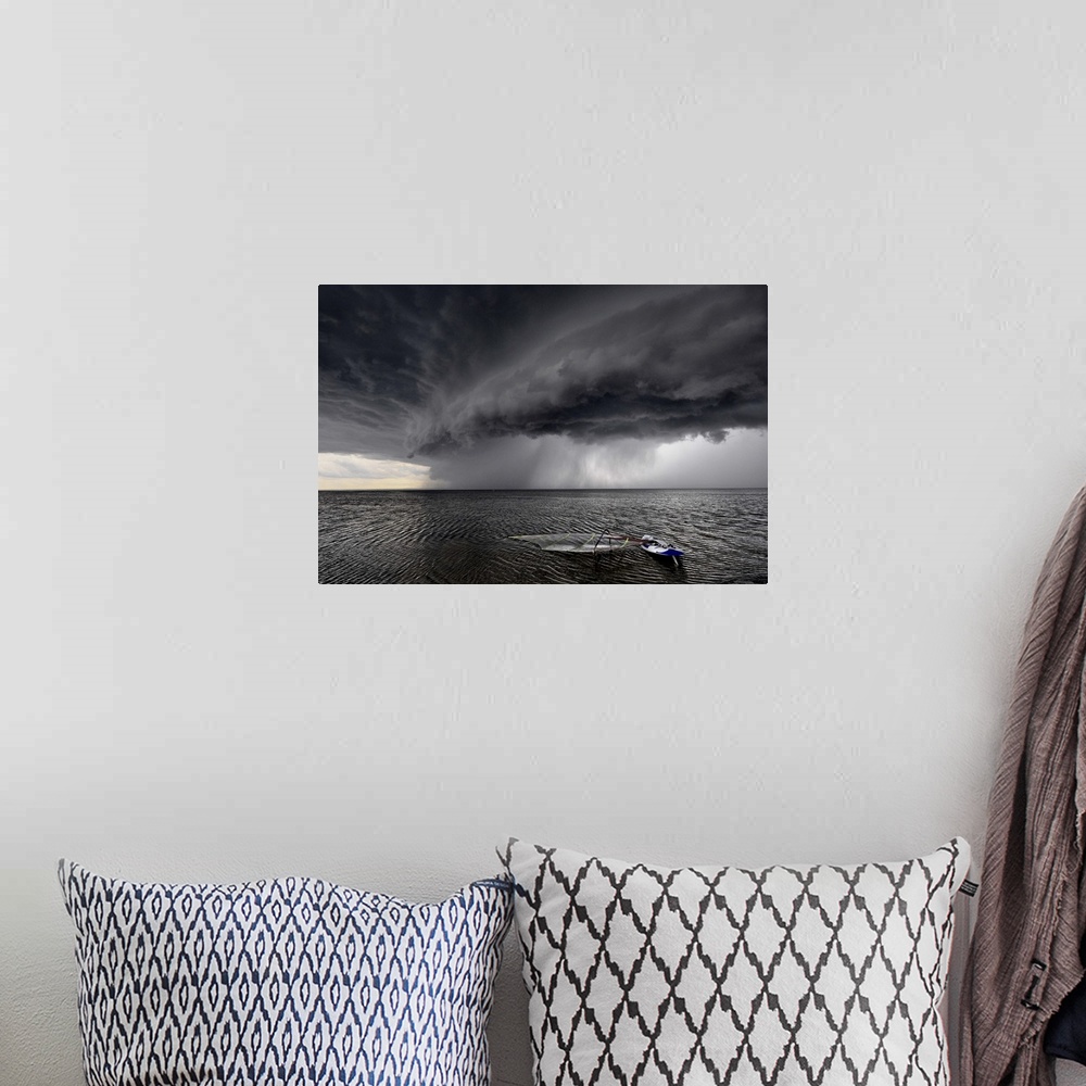 A bohemian room featuring A windsurfing board lays flat in the water as stormclouds with heavy rain approach.