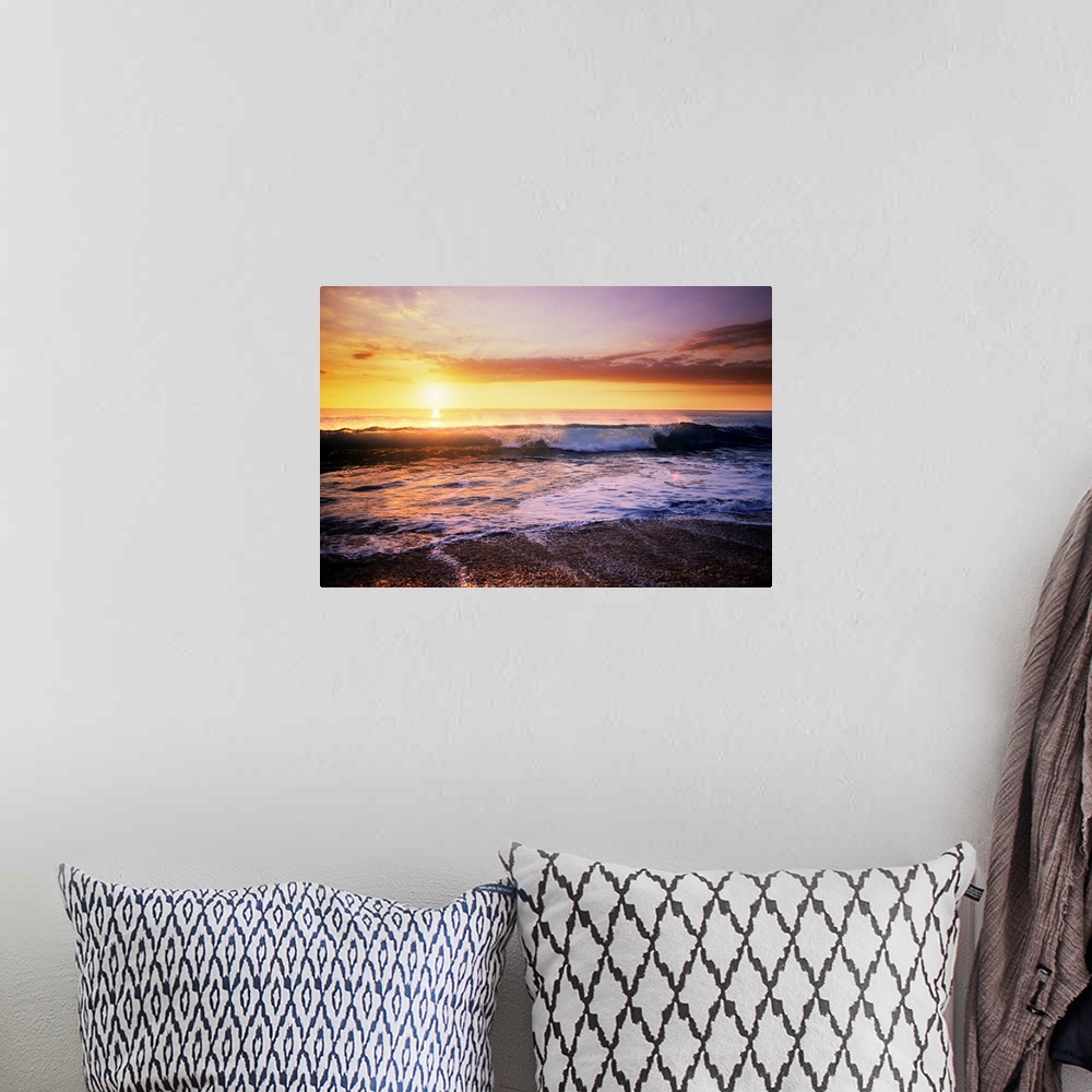 A bohemian room featuring The sun is setting in the distance over the ocean as a wave begins to crash near the edge of the ...