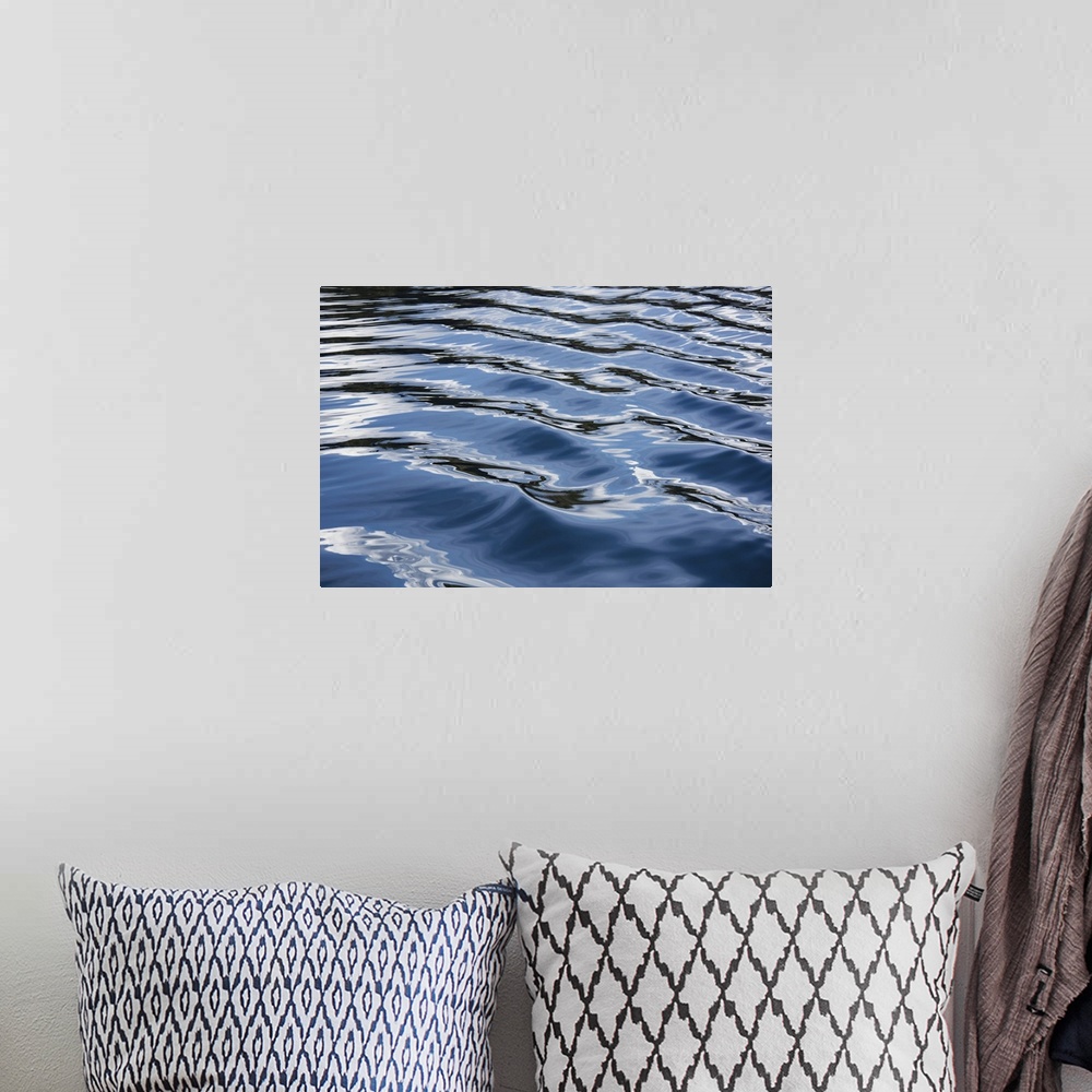 A bohemian room featuring The blue, black, and white reflections of the sky, clouds, and nearby land on the wake of a boat ...