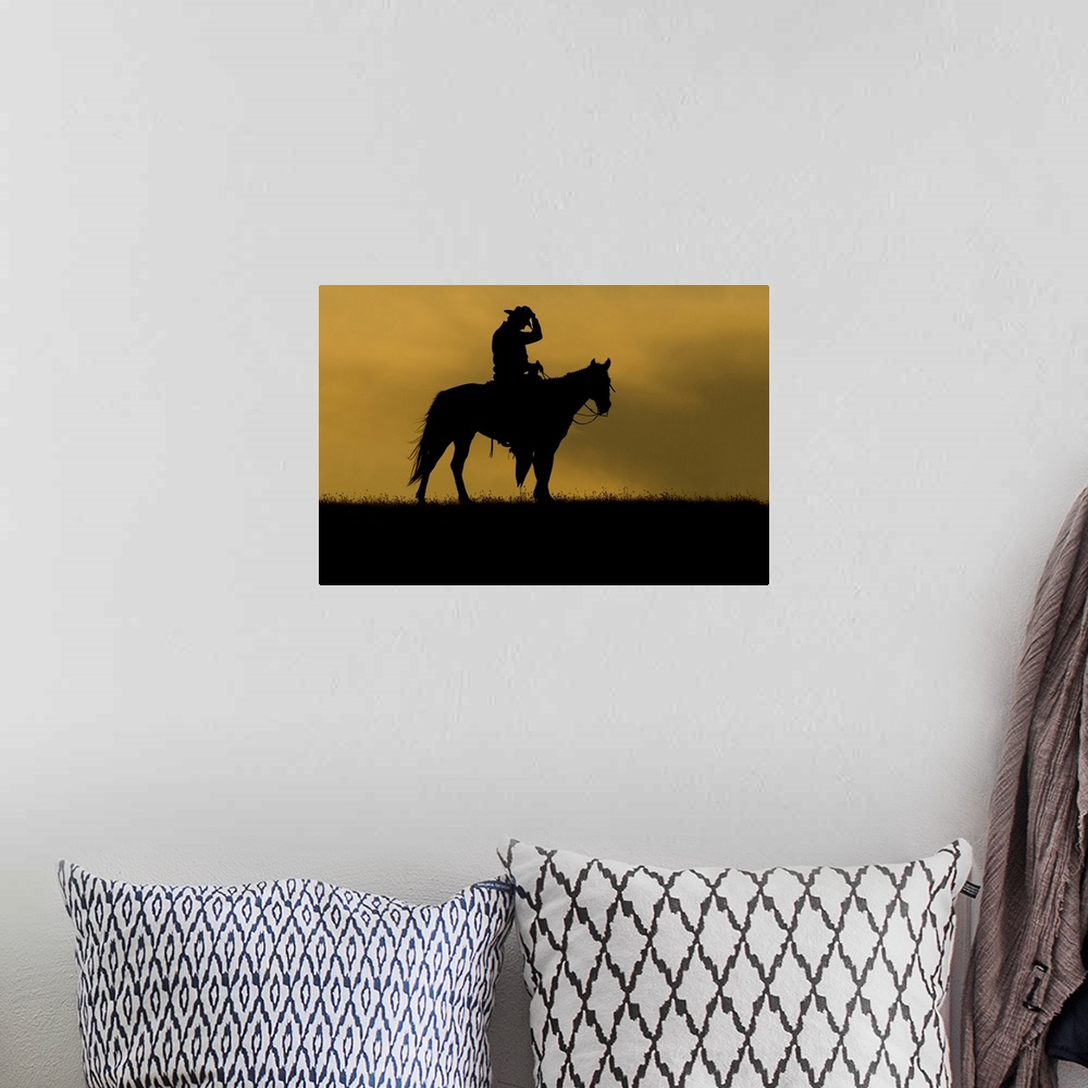 A bohemian room featuring Silhouette of a cowboy on a horse against a sky of golden cloud at sunset; Montana, United States...