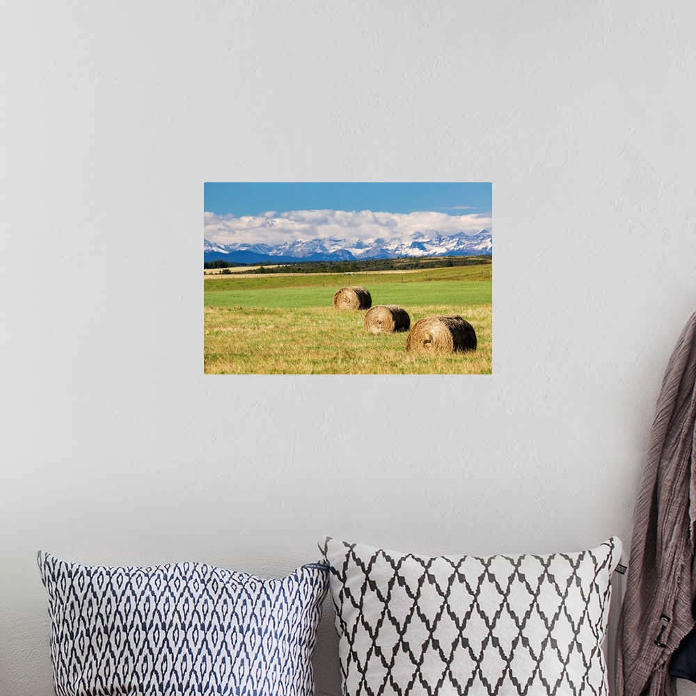 A bohemian room featuring Three hay bales in a field with mountains in the background slightly snow covered and cloudy with...