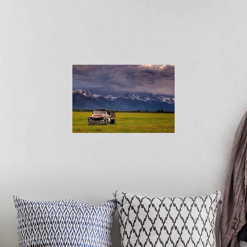 A bohemian room featuring Landscape photograph of a yellow-green field with an old rusted truck and snow capped mountains i...