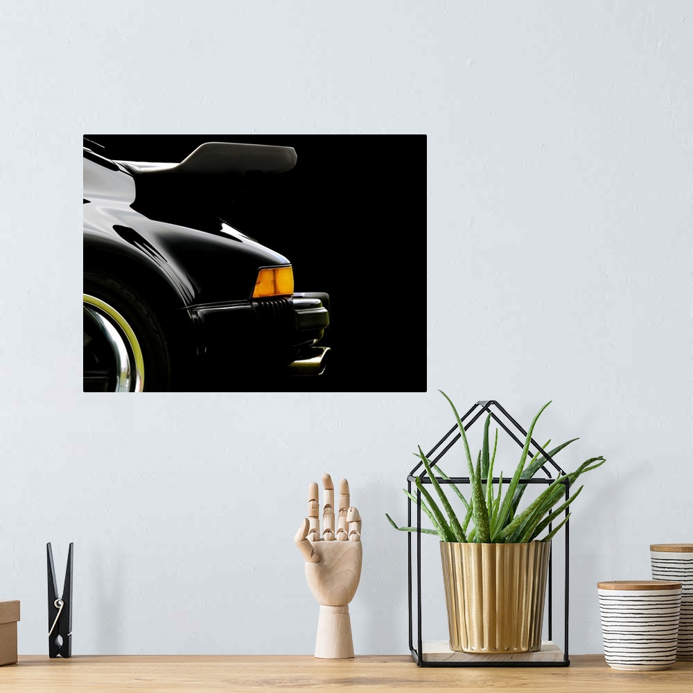 A bohemian room featuring Photograph of the rear and back wing of a black 78 Porsche 930 with a solid black background.