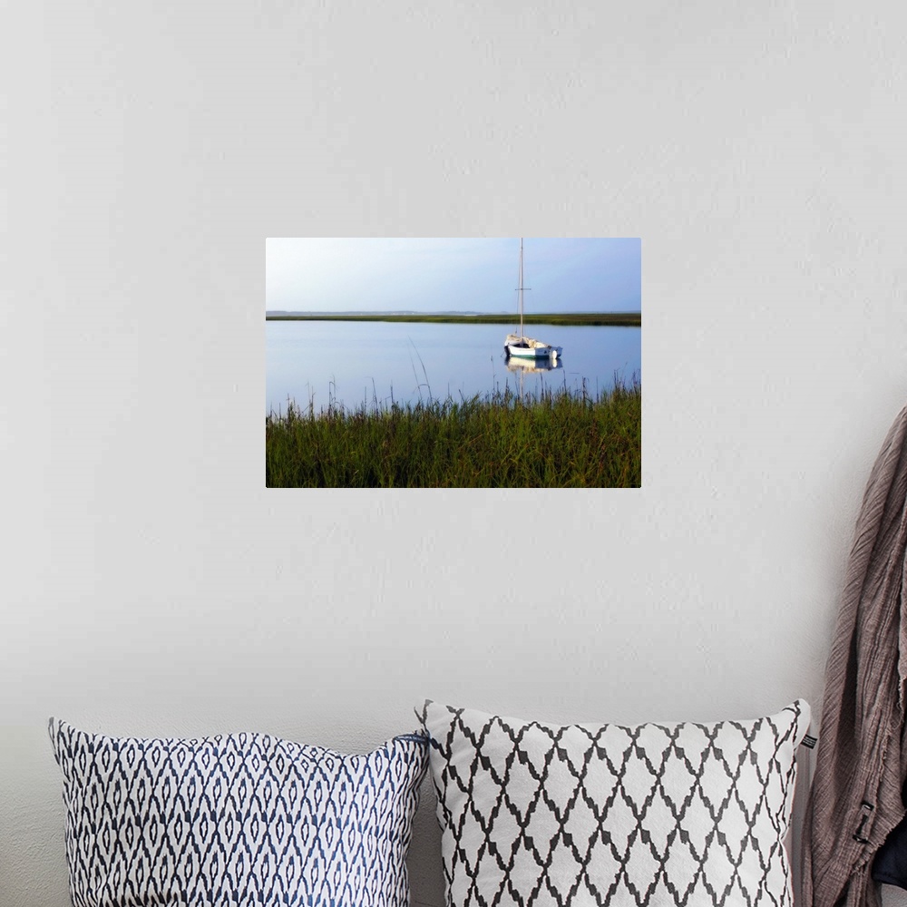 A bohemian room featuring A landscape photograph of a sailboat anchored in still waters surrounded by marshy grasses on the...