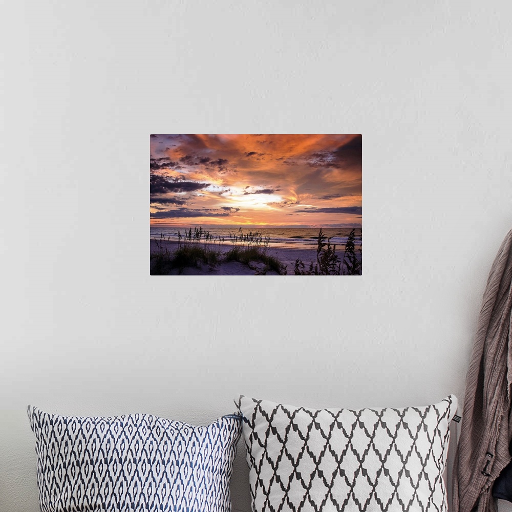 A bohemian room featuring Cloudy sky at sunrise glowing orange over the beach.