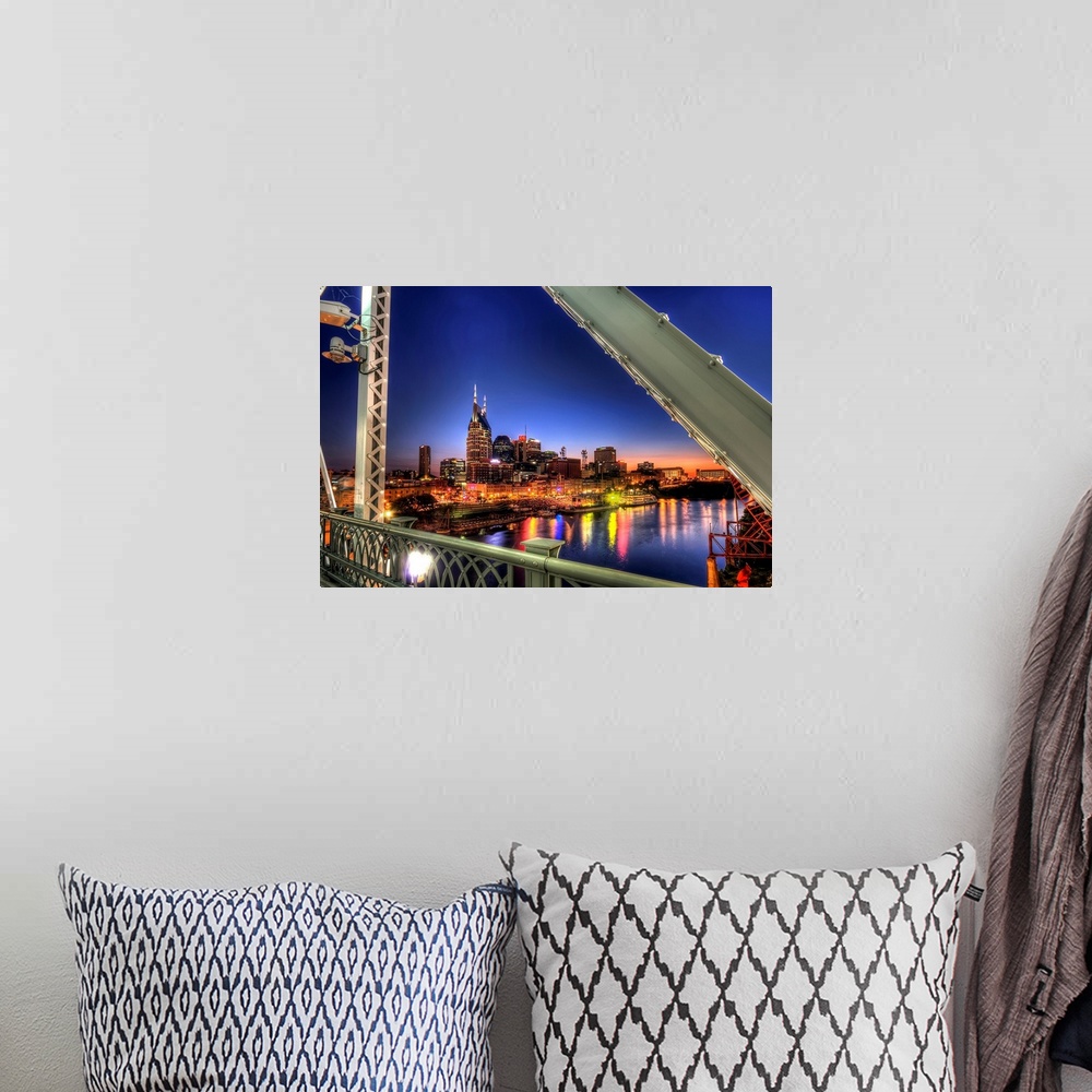 A bohemian room featuring Large wall docor overlooking a lit up downtown cityscape from a bridge at dusk with a river runni...