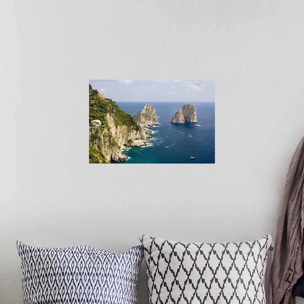 A bohemian room featuring Large rock formations stand in the water next to an immense cliff off the Italian coast.