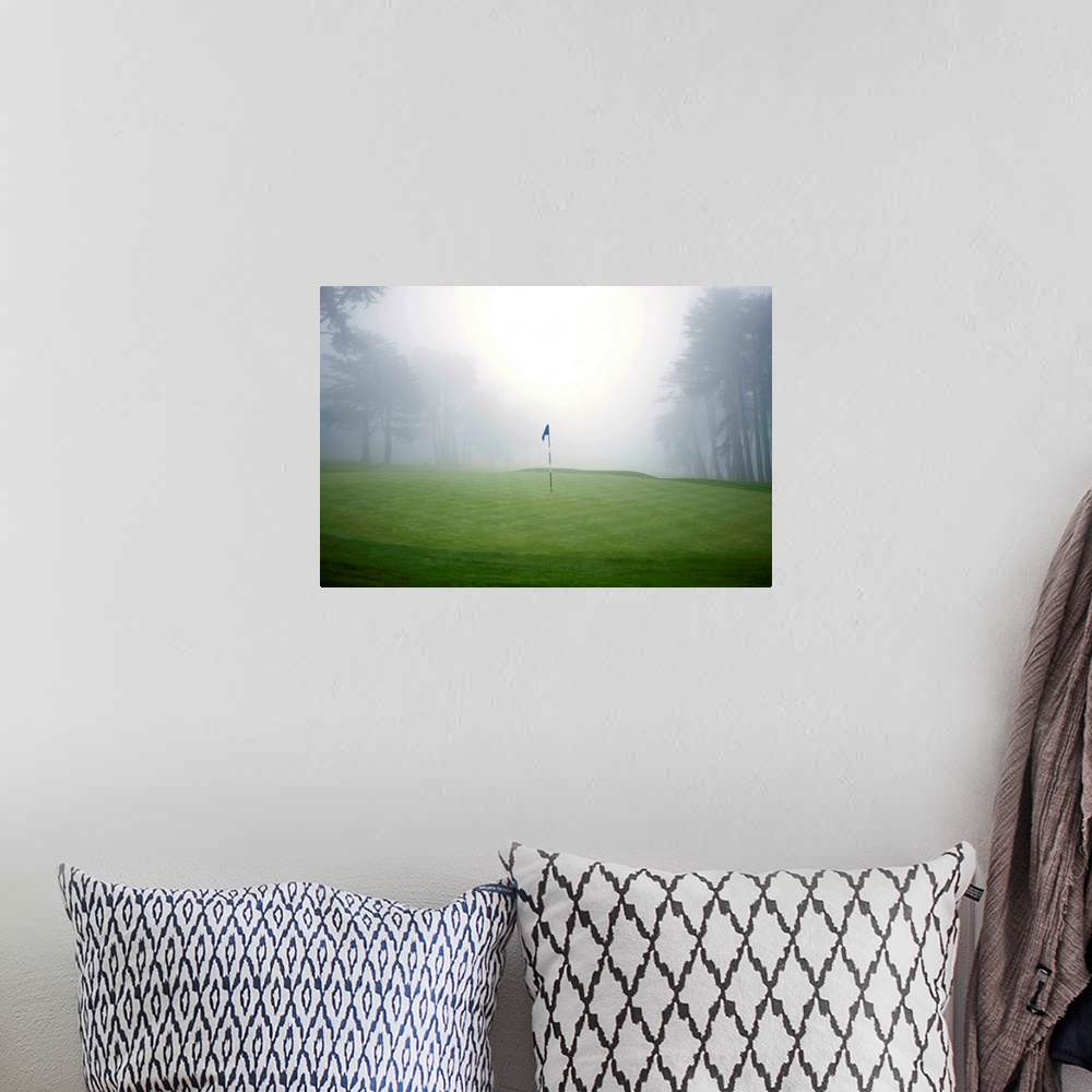 A bohemian room featuring Flag on putting green on golf course, fog and trees in background