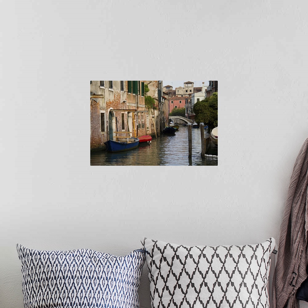 A bohemian room featuring A picture of a canal is taken with boats docked on the left side where buildings line the water.