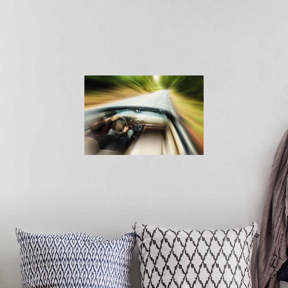 A bohemian room featuring lifestyle photograph of a caucasian man driving fast down a road in a convertible