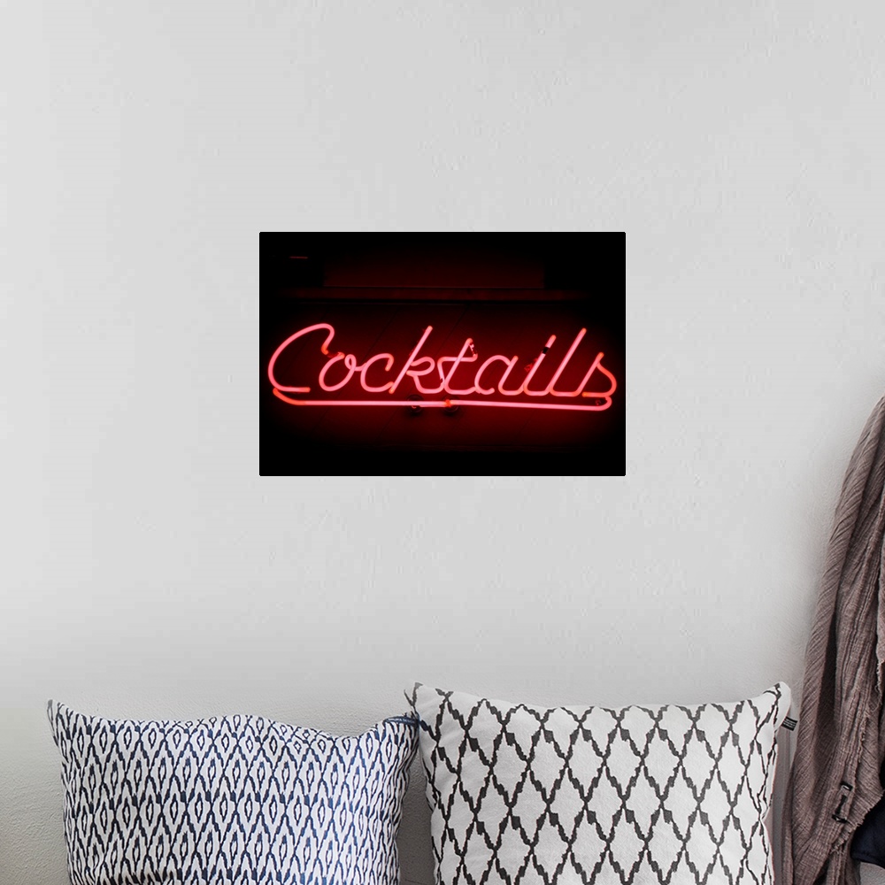 A bohemian room featuring An illuminated pink sign with the work cocktails sits on a dark wall.
