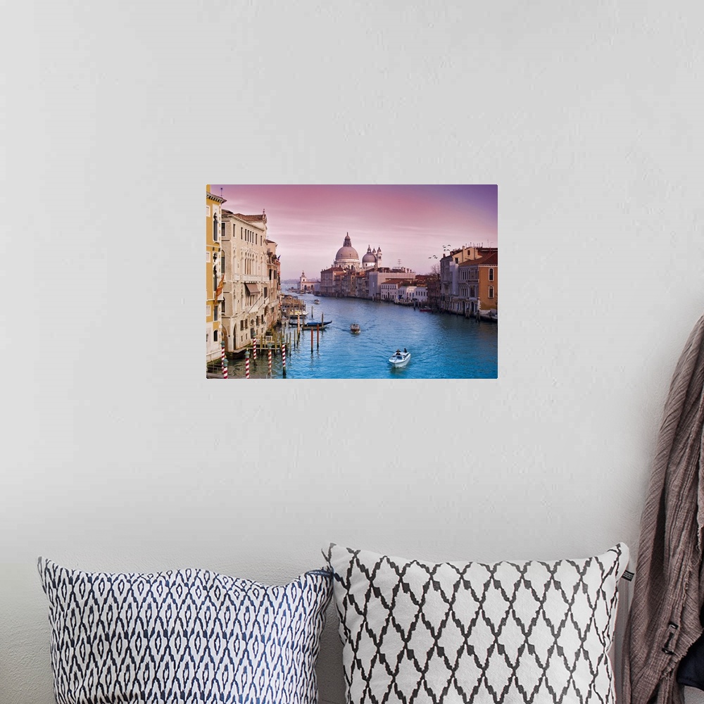 A bohemian room featuring Wall art of buildings on either side of an Italian canal with boats floating through the water.