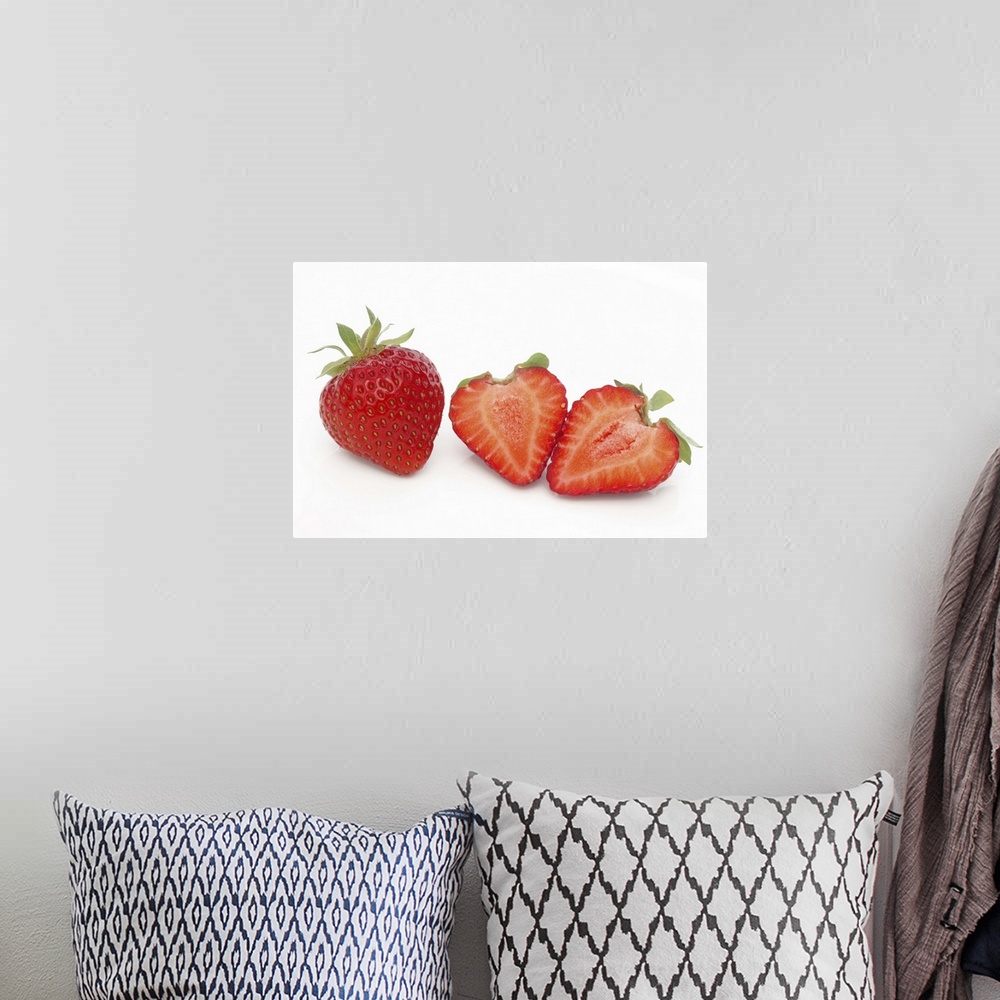 A bohemian room featuring Two fresh, ripe, home grown, organic strawberries, one cut into two halves, on a white background.