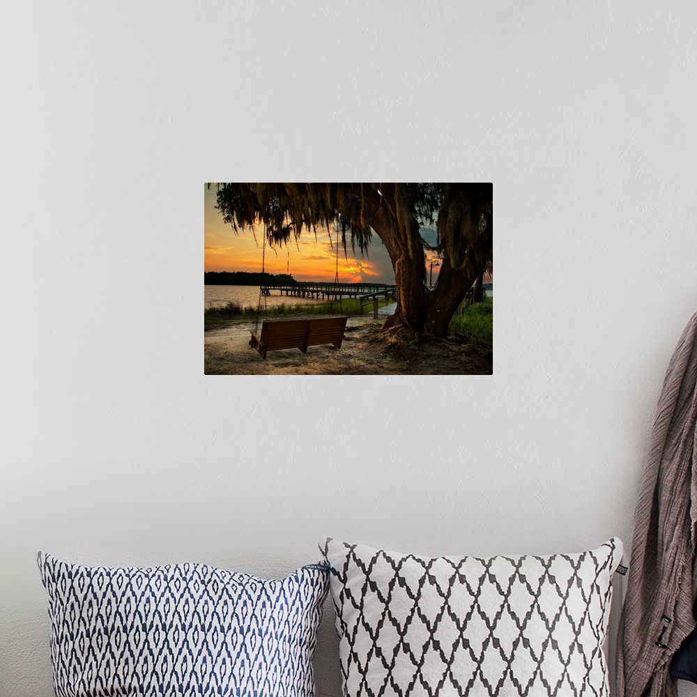 A bohemian room featuring A vibrant photograph of bench swing tethered to a dropping tree, looking out over a lake at sunset.