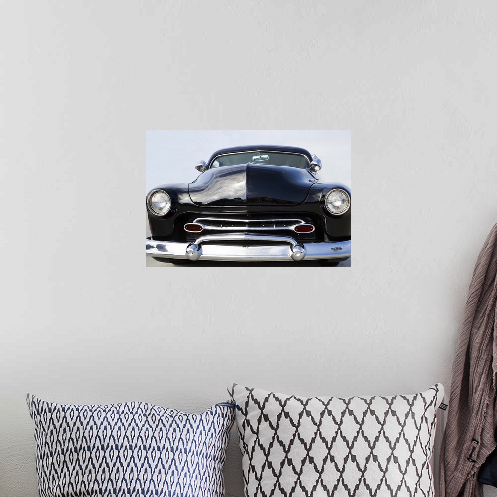 A bohemian room featuring The front of a classic car with a chrome bumper and dark paint.