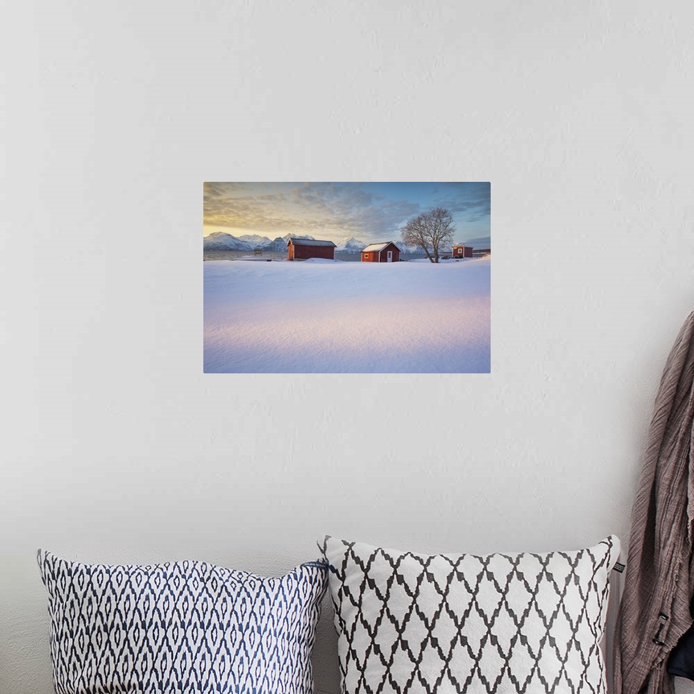 A bohemian room featuring The orange sky at sunset frame the frozen sea and typical Rorbu immersed in the snow Djupvik Lyng...