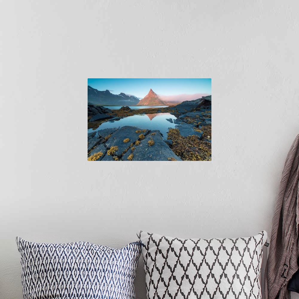 A bohemian room featuring The rocky peak of Volanstinden lighted up by the midnight sun is reflected in blue sea Fredvang L...