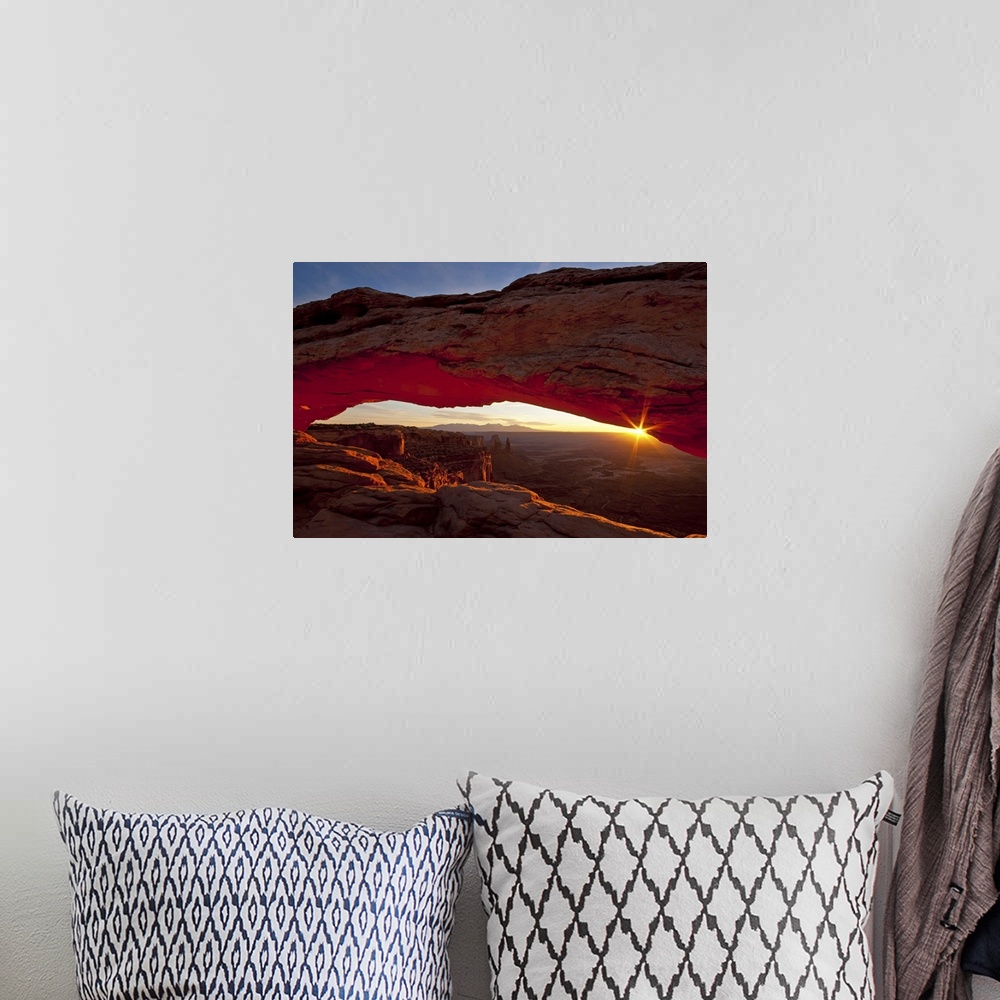 A bohemian room featuring A photograph is taken through the mesa arch as the sun begins to rise over the horizon.
