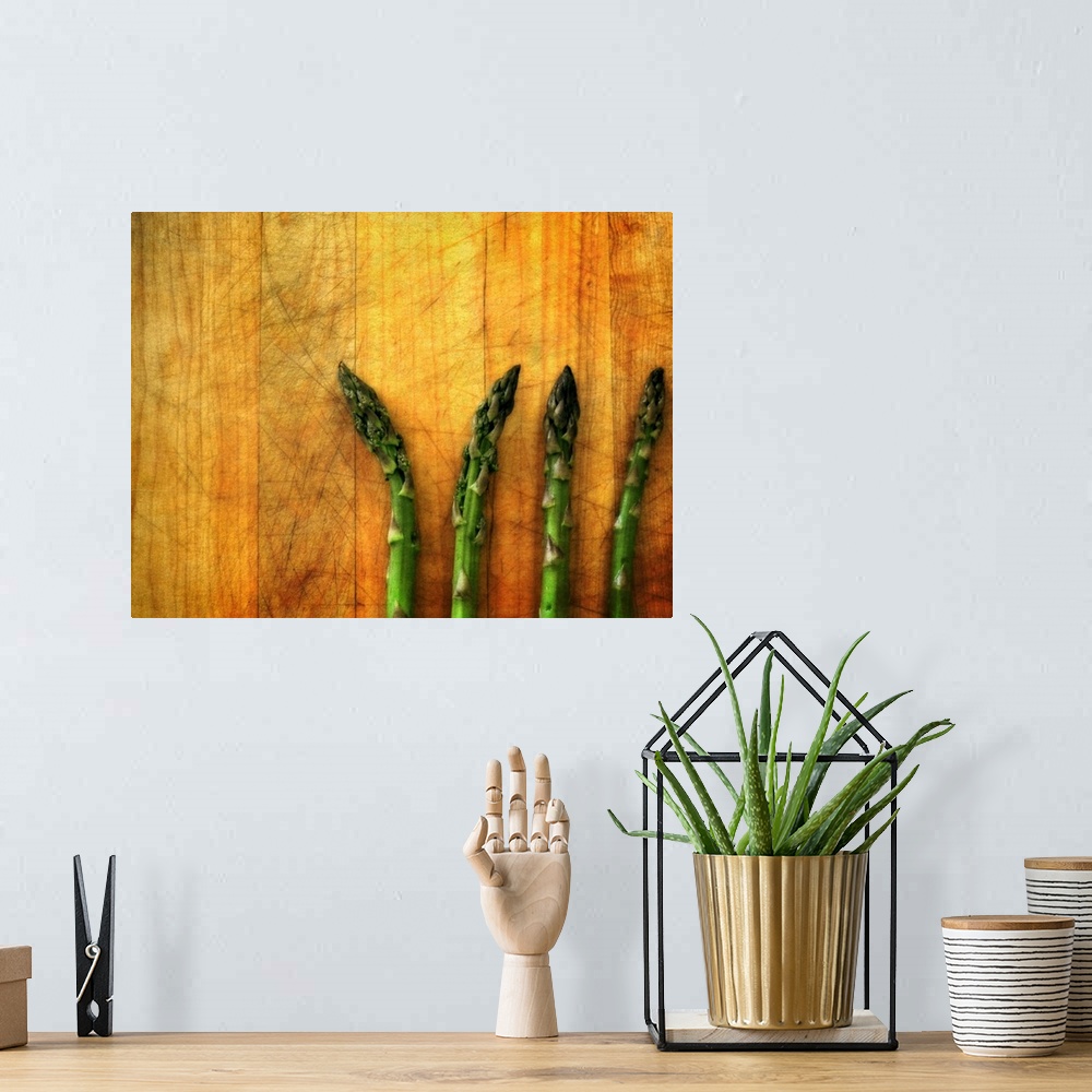 A bohemian room featuring Four green asparagus spears laying on a wooden surface.