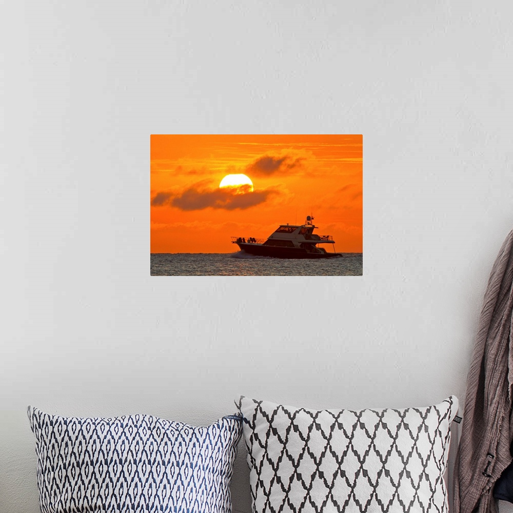 A bohemian room featuring Boat passing in front of a big glowing sun during a spectacular sunset over the Atlantic Ocean.