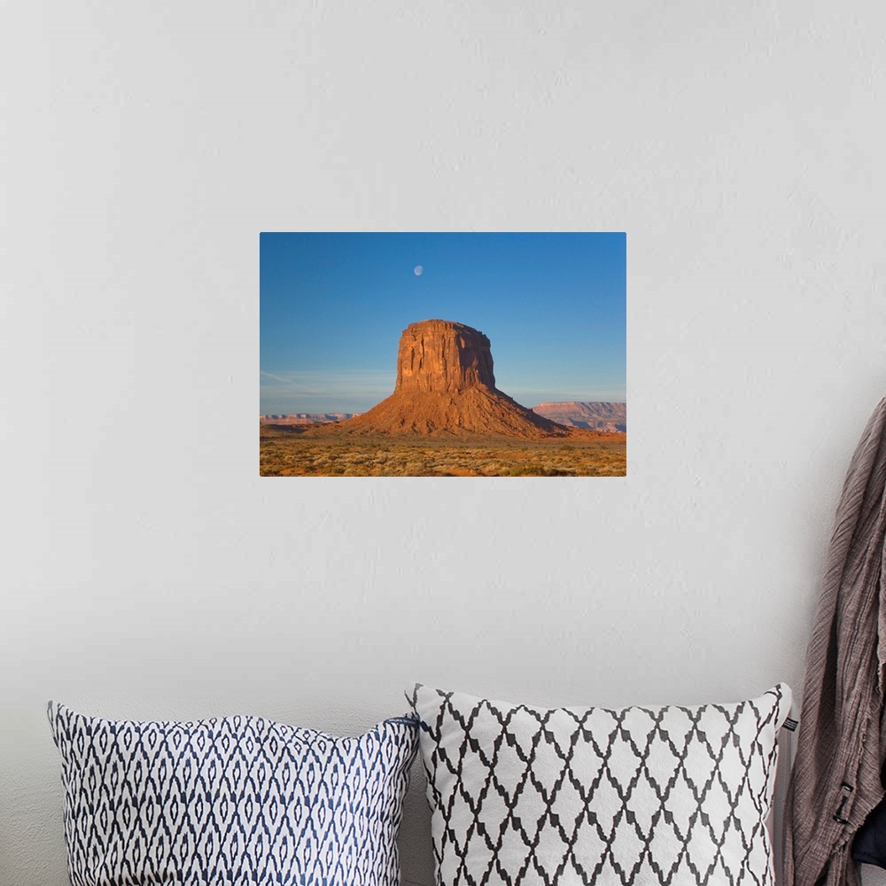 A bohemian room featuring Moon visible over rock formation in Monument Valley in early morning.