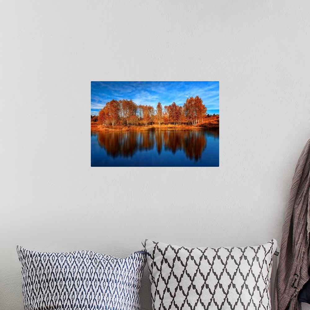 A bohemian room featuring Bright orange trees reflected in the deep blue water of a lake.