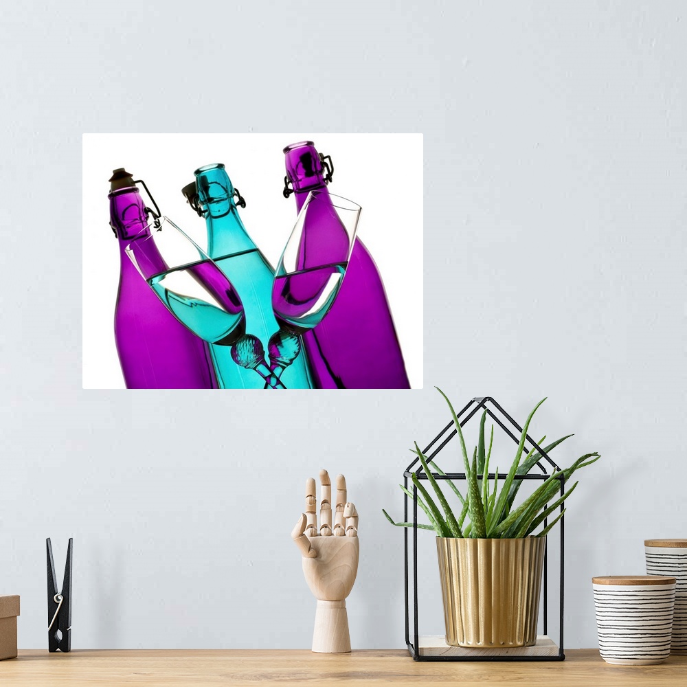 A bohemian room featuring turquoise and purple glass bottles with two champagne flutes crossing in front on a white backgro...