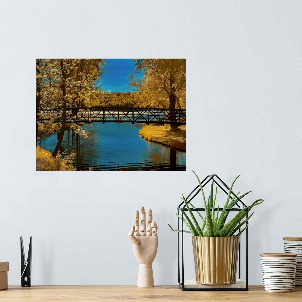 A bohemian room featuring Long bridge over a river lined with Autumn colored trees and grass.