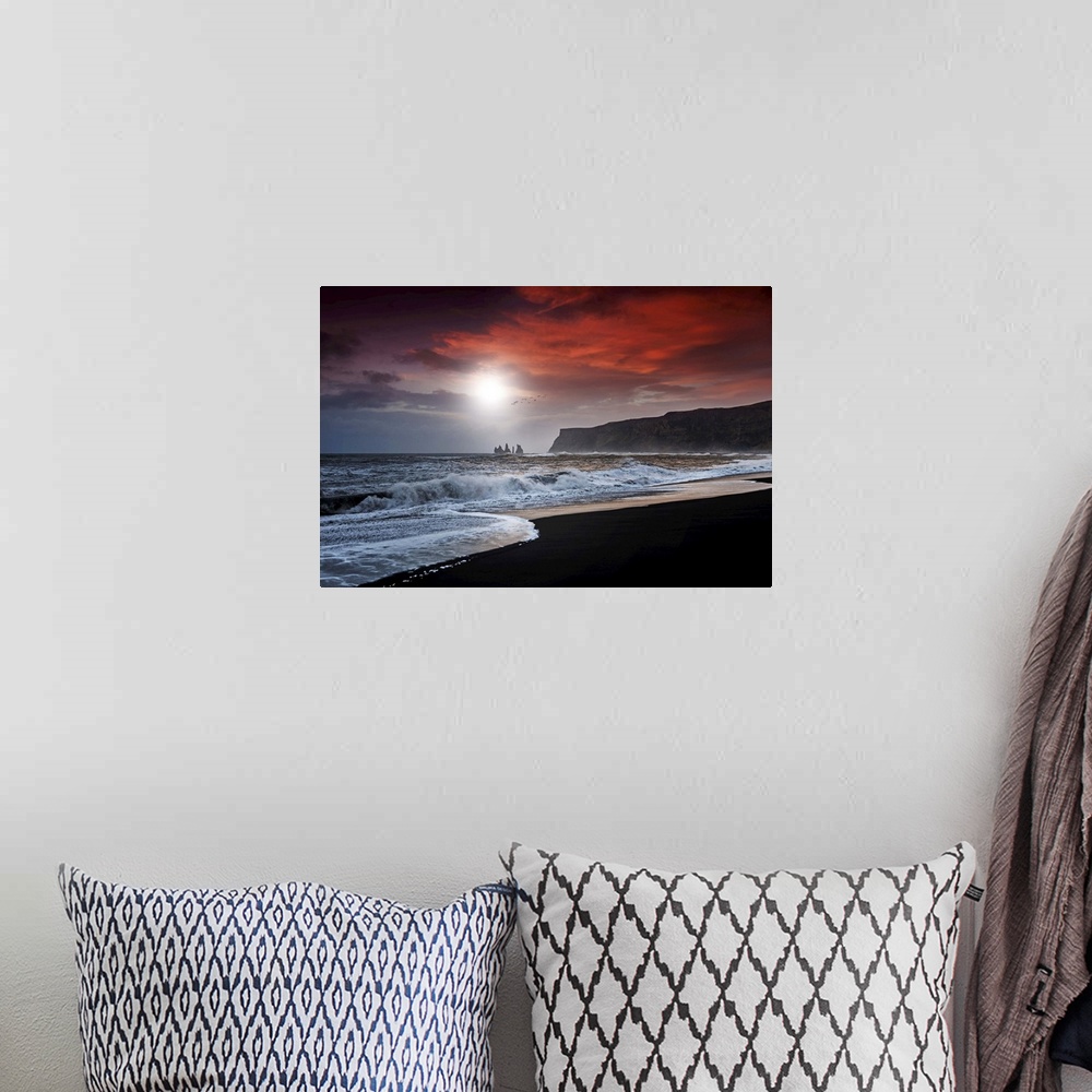 A bohemian room featuring A photograph of a dark coastline under a red clouds.