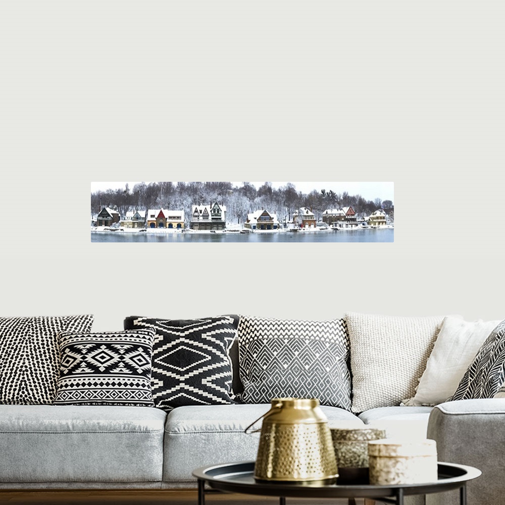 A bohemian room featuring Snow covered houses sit right on the edge of a river. Trees and the ground behind them are covere...