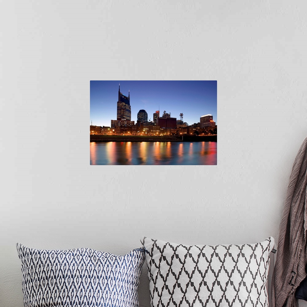 A bohemian room featuring This photograph city skyline lit up in the early twilight and the city lights reflect in the water.