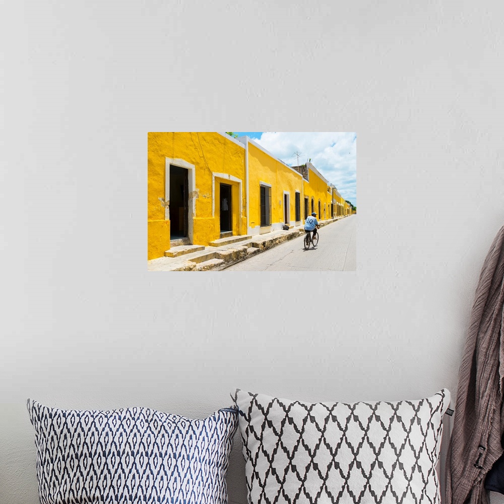 A bohemian room featuring Pphotograph highlighting the yellow buildings in Izamal, Yucat?n, Mexico, with a man in blue ridi...