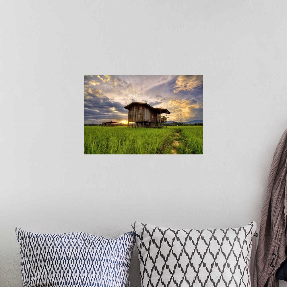 A bohemian room featuring An old wooden building in a field under a colorful sunset sky.