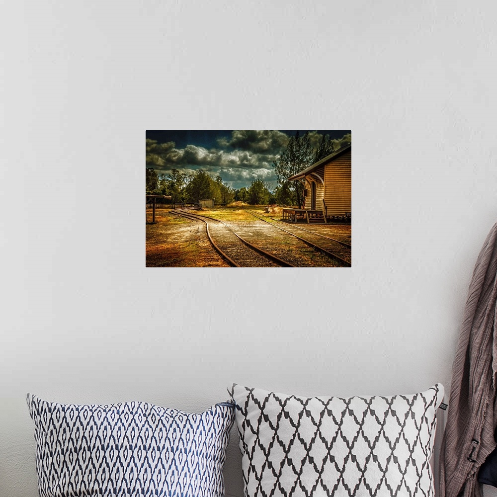 A bohemian room featuring Train tracks through a village under dark clouds.