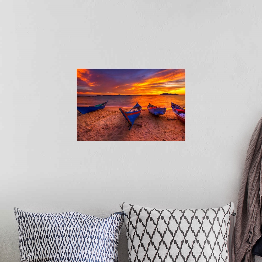 A bohemian room featuring A row of small blue boats resting on the sandy beach with a brilliant sunrise.