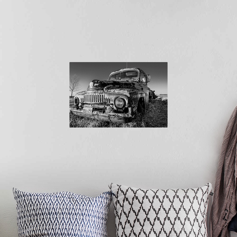 A bohemian room featuring A black and white image of an old pick-up truck slowly sinking in the grass of an old farm yard a...