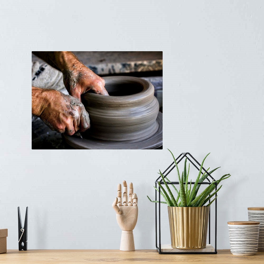 A bohemian room featuring A sculptor's hands shaping a round clay pot on a spinning wheel.